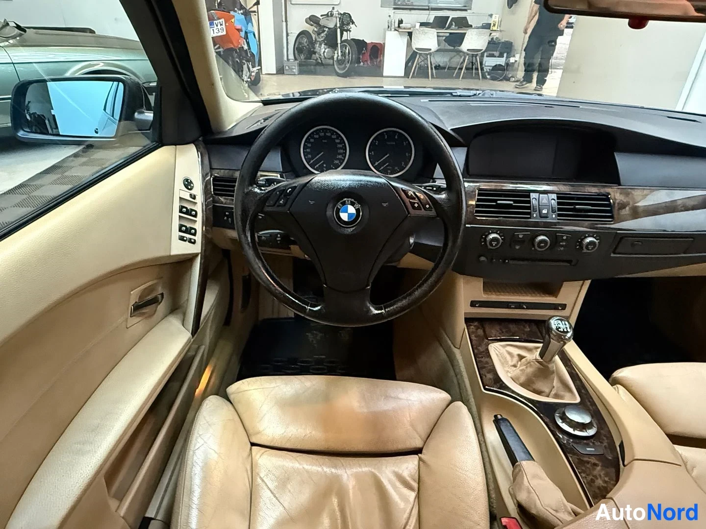 Yksityiskohta: Auton sisätila ohjaamosta nähtynä: BMW-ohjauspyörä, analogiset mittarit, manuaalivaihteisto ja beige nahkapenkit.