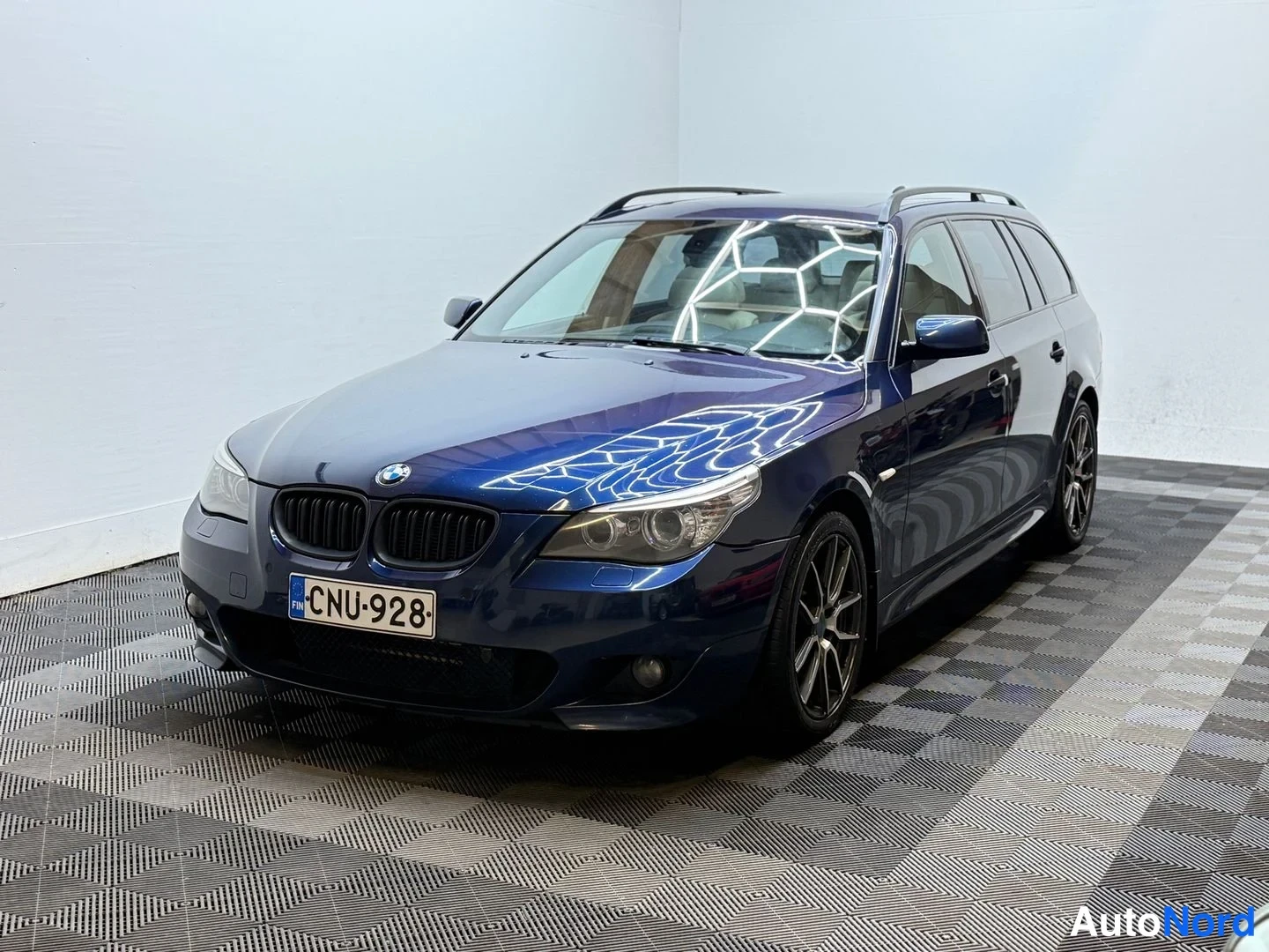Etuviisto, nokka vasemmalle: Tummansininen BMW-farmari kolmostietä, rekisterikilpi, katto­kaiteet ja tummat kevytmetallivanteet näkyvät.
