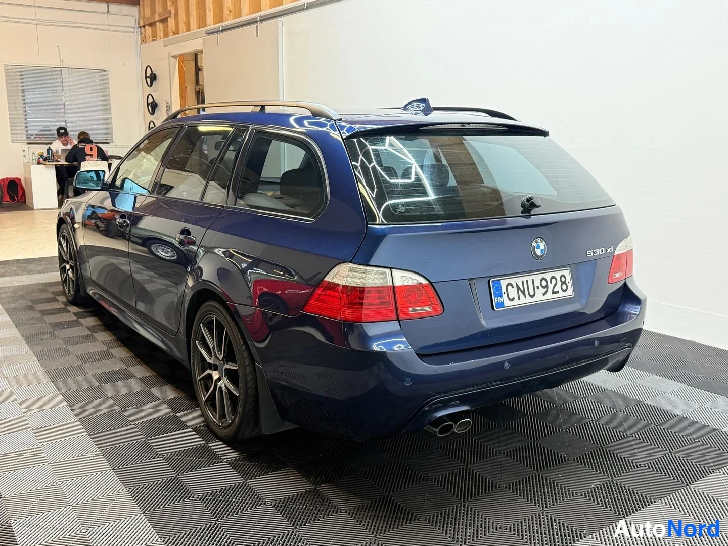 Takaviisto: Tummansininen farmariauto takaa sivulta kuvattuna autotallissa, rekisteritunnus, kattokaiteet, perävaunun vetokoukkualue ja kaksi pakoputkea.
