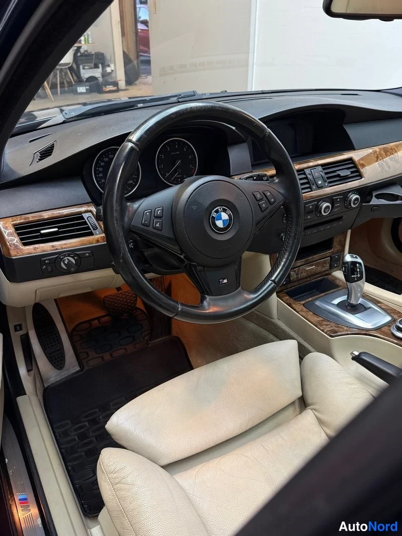 Etuviisto, nokka vasemmalle: Kuljettajan puolen sisätila: BMW-ohjauspyörä, mittaristo, puukuvioinen paneeli, automaattivaihteiston valitsin ja beige-pohjainen istuin.