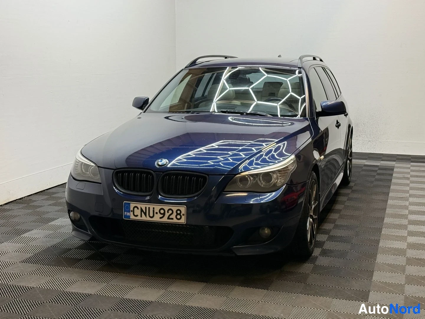 Etuviisto, nokka vasemmalle: Tummansininen BMW etusivulta vasempaan viistosti sisätilassa, rekisterikilpi.