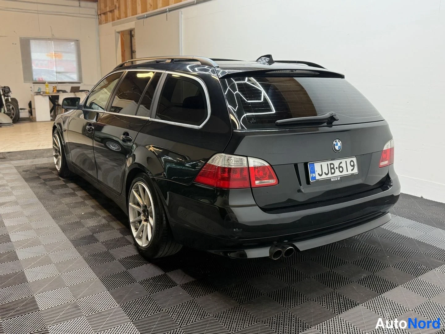 Takaviisto: Mustan farmariajon takaosan kolmeneljänneskuva vasemmalta; rekisteritunnus, BMW-merkki, kaksoispakoputki ja kattokaiteet näkyvät.