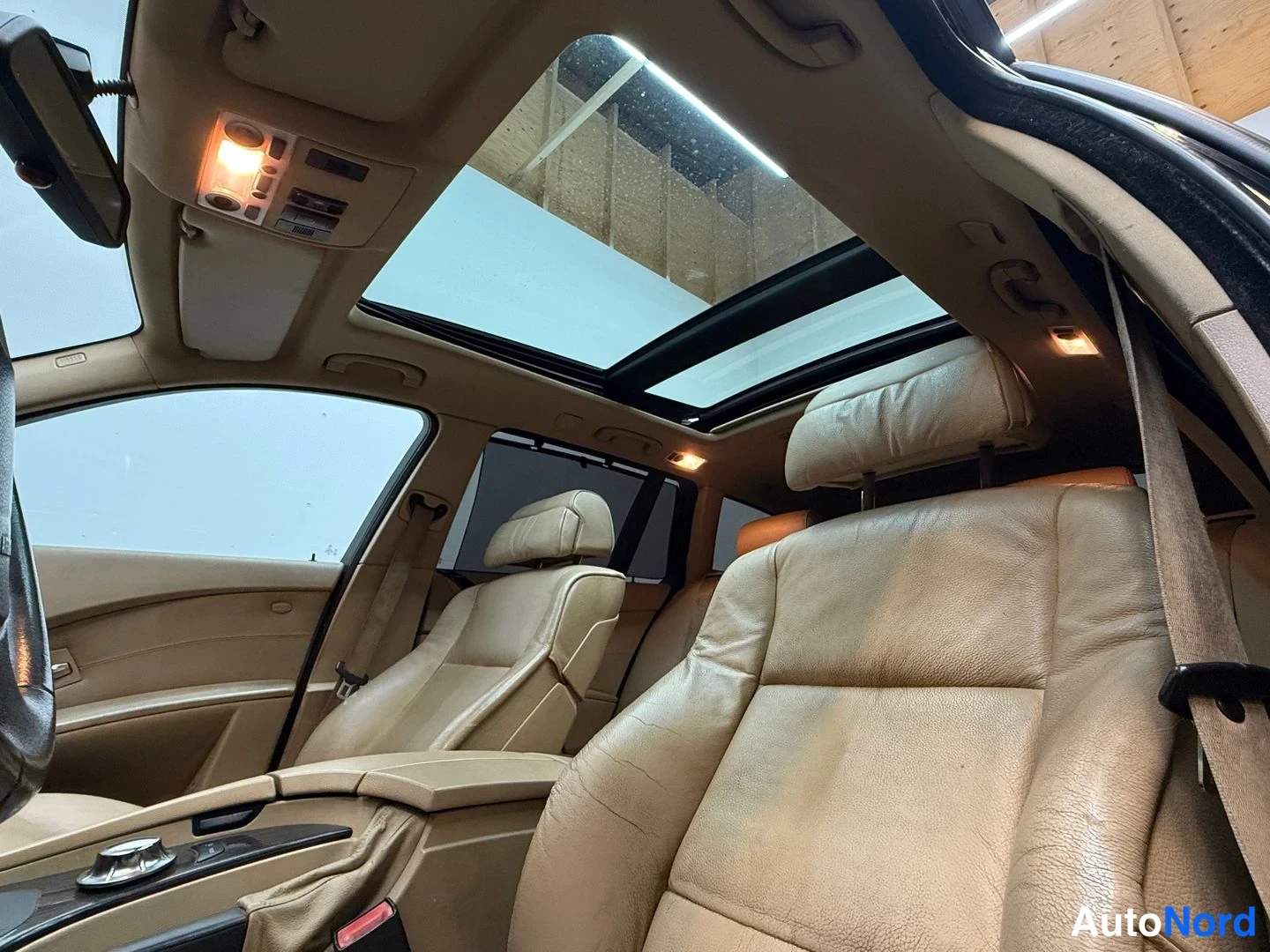 Muu: Sisätilakuva: panoraamakatto, beige/tan nahkaiset etuistuimet, takapään niskatuet ja iDrive-ohjainnäppäin keskikonsolissa.