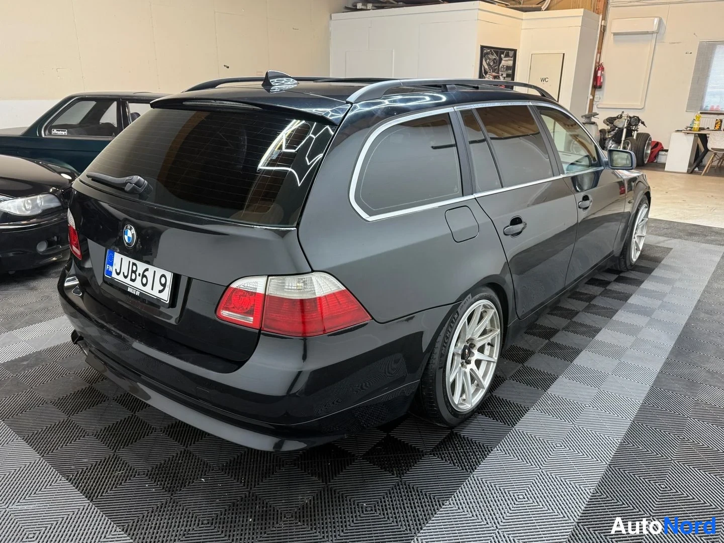 Takaviisto: Mustan farmariajon takaosan kolmeneljänneskuva oikealta; rekisteritunnus, BMW-merkki takaluukussa, kattokaiteet ja hopeavanteet näkyvät.