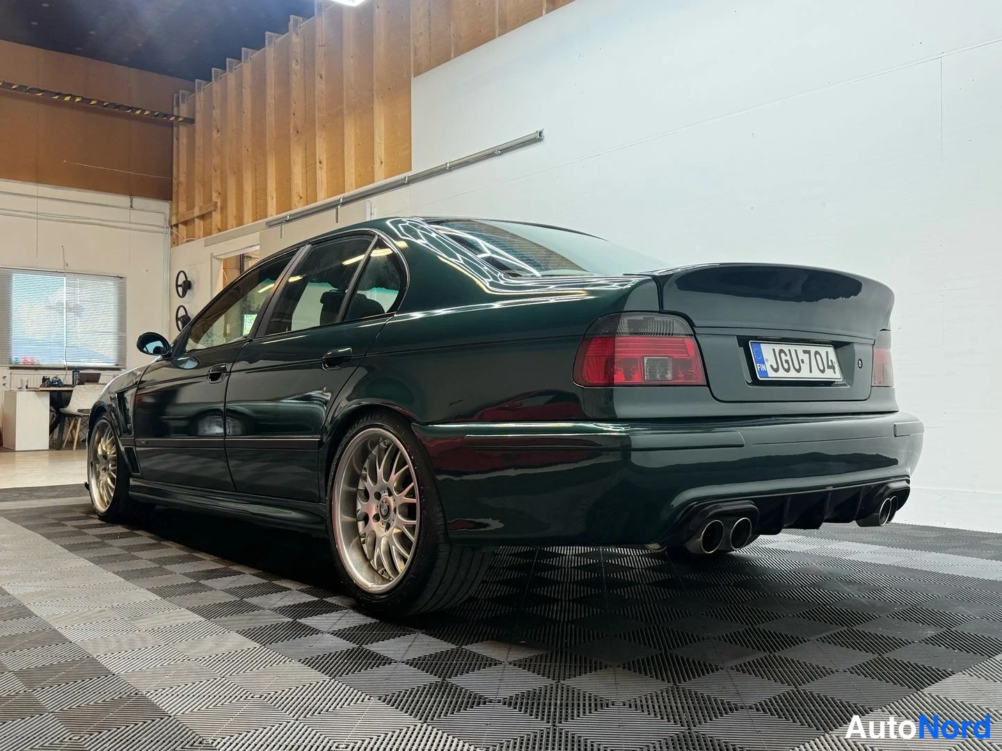 Takaviisto: Tummansininen BMW-sedan, perä vasemmalle, tallissa tai varikolla ja valaistu.