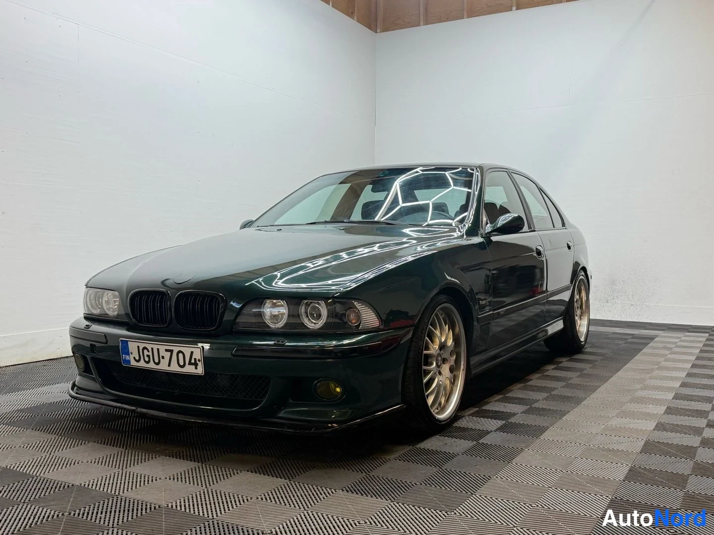 Etuviisto, nokka vasemmalle: Tummansininen BMW-sedan, nokka vasemmalle, konepelti ja ovet näkyvät.