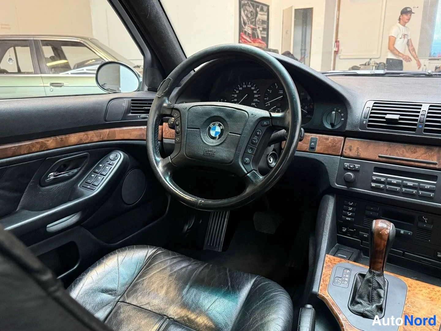 Muu: Ohjaamo vasemmalta: BMW-ohjauspyörä, analogiset mittarit, tumma puukoristelistat ja valohihtiset nahkaistuimet, automaattivaihteen valitsin.