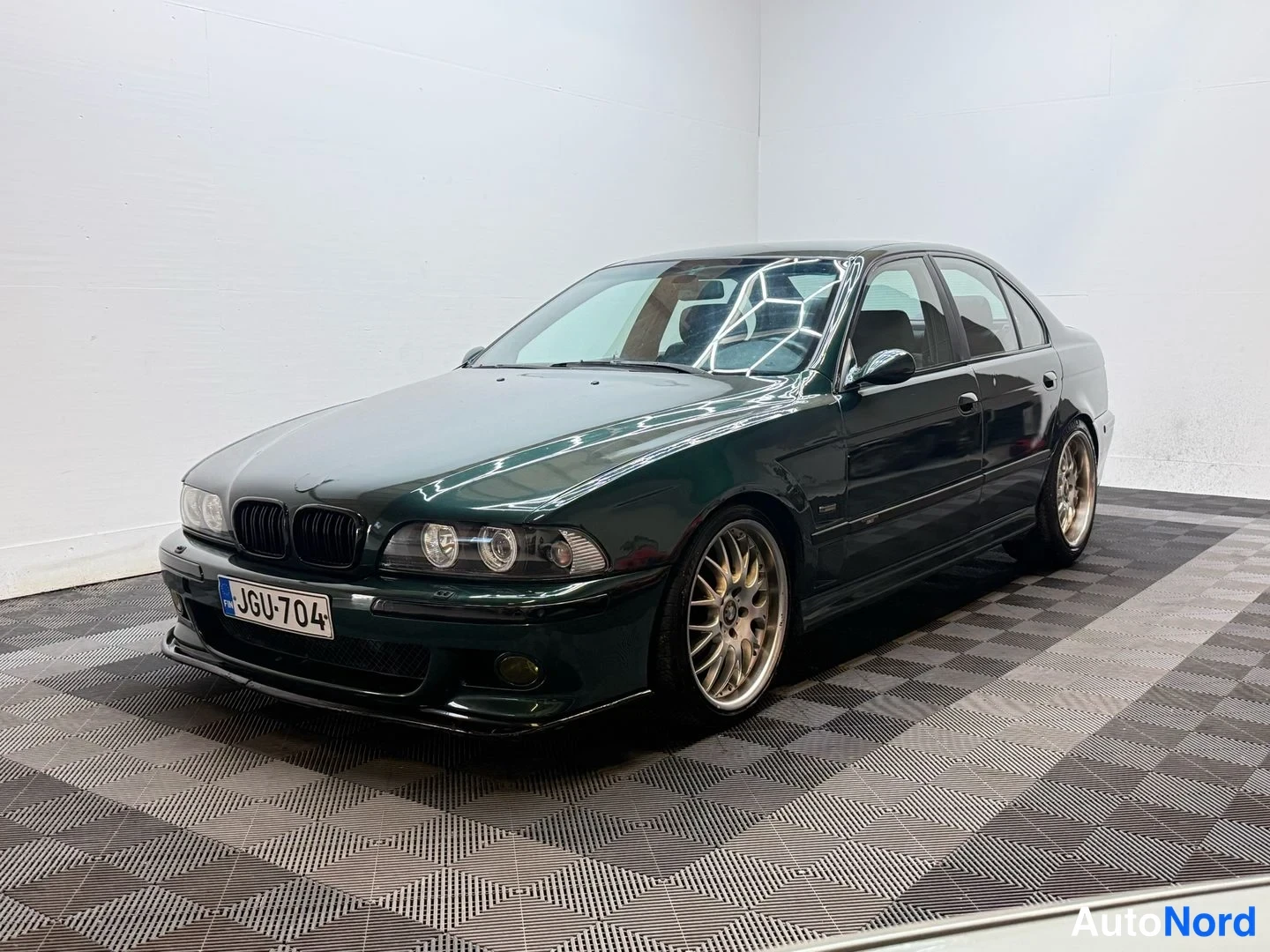 Etuviisto, nokka vasemmalle: Tummansininen BMW-sedan, nokka vasemmalle, tallissa, kirkas valaistus.