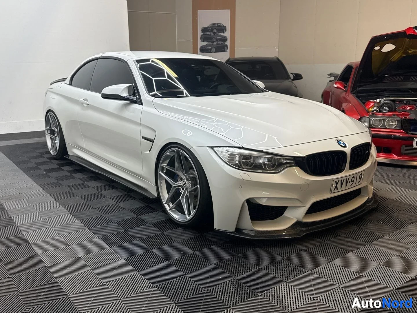 Etuviisto, nokka oikealle: Valkoinen BMW-avolava-auto kolmannelta kulmaltta etuosasta oikealle, rekisteritunnus, hallitilassa.
