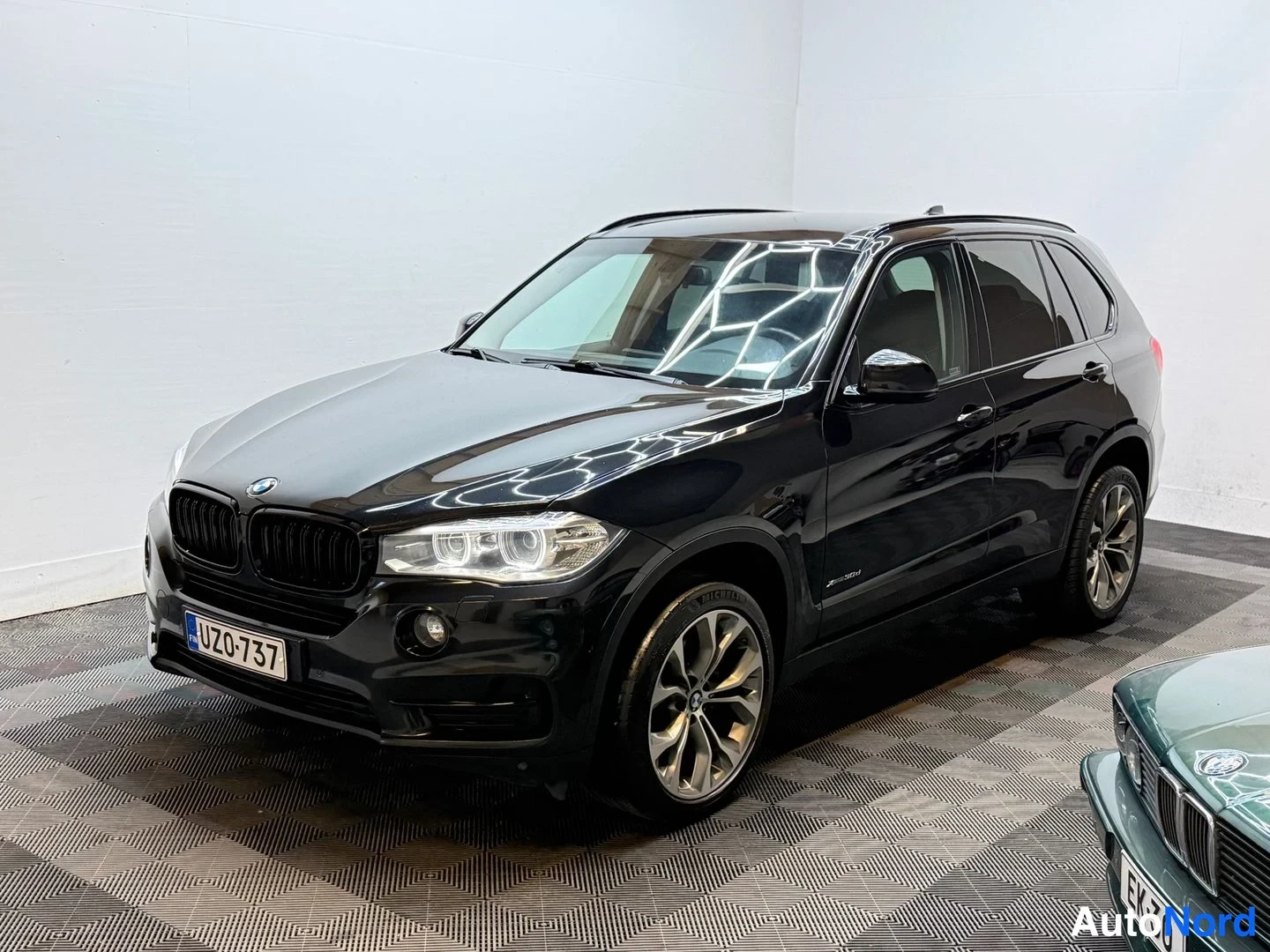 Etuviisto, nokka vasemmalle: Musta BMW X5farmari kulmassa edessä vasemmalla, rekisteritunnus näkyvissä.