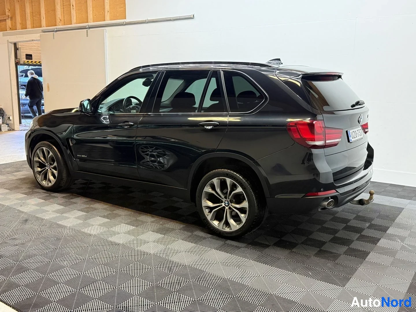 Takaviisto: Mustan BMW X5:n takaosa ja kylki kolmivartalokulmassa, rekisterikilpi, kevytmetallivanteet ja vetokoulu näkyvissä.