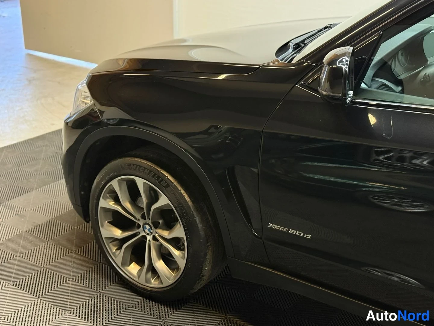 Etuviisto, nokka vasemmalle: BMW X5:n etukolmasosakuva: musta konepelti, etuvanne MICHELIN-renkaalla ja 'X5 xDrive 30d' -merkintä ovessa.