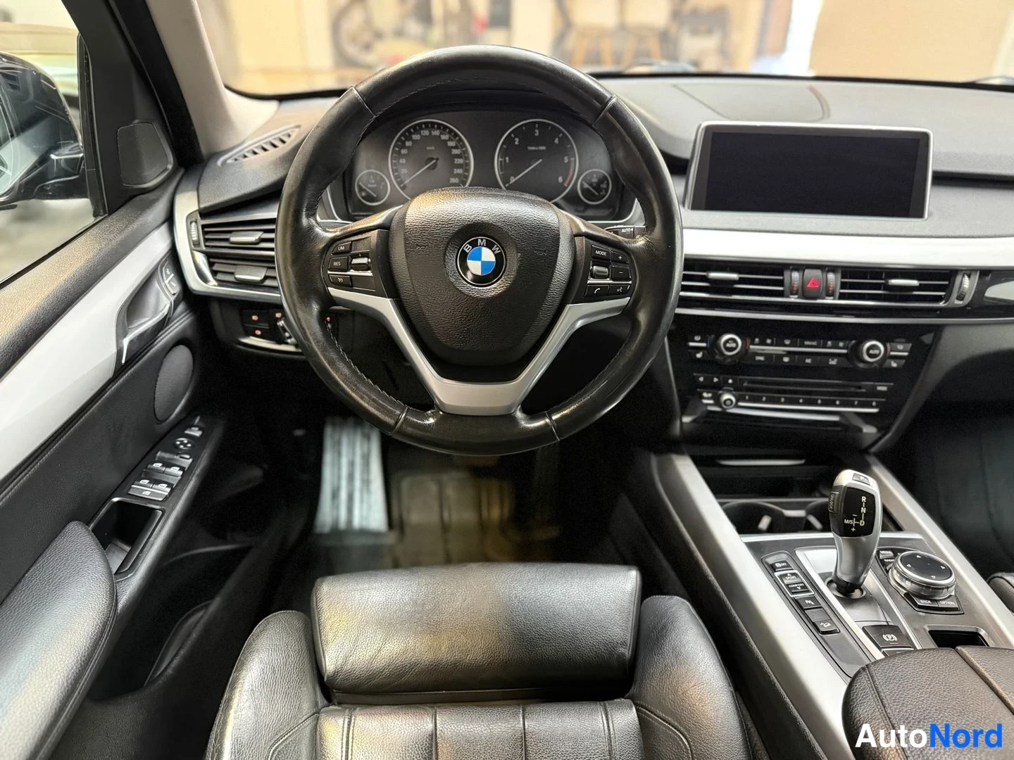 Edestä: Ohjaamosta kuvattu näkymä: BMW-merkkinen ohjauspyörä, mittaristo ja keskikonsolin näyttö.