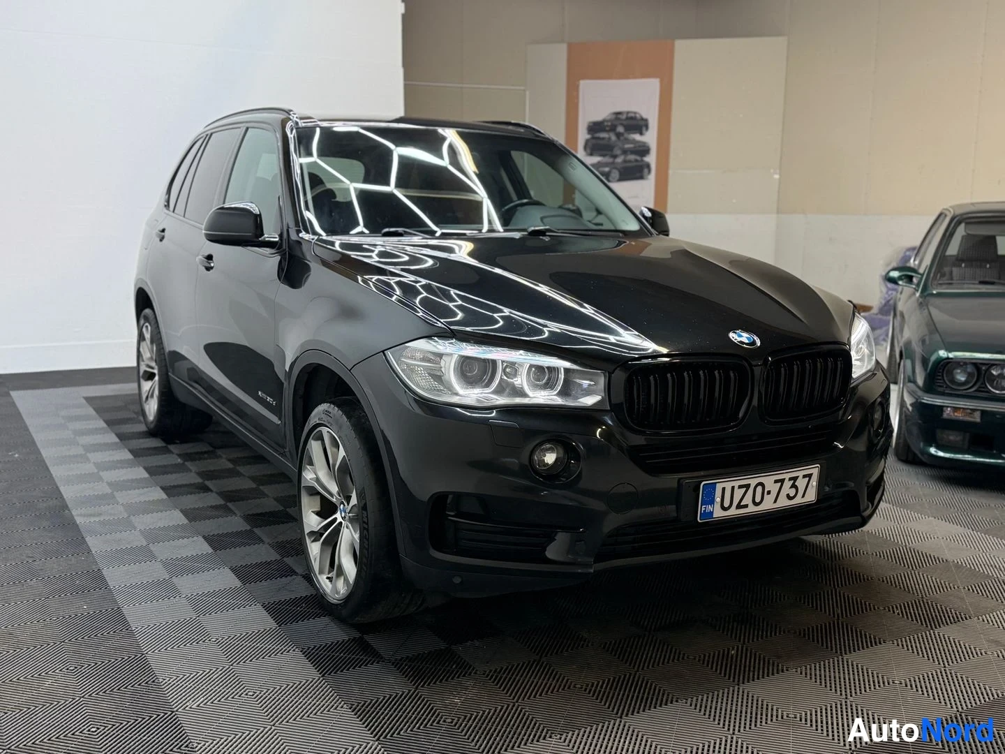 Etuviisto, nokka oikealle: Mustan BMW X5:n etukulma vasemmalta edestä kuvattuna; etupanssarissa lukee rekisteritunnus.