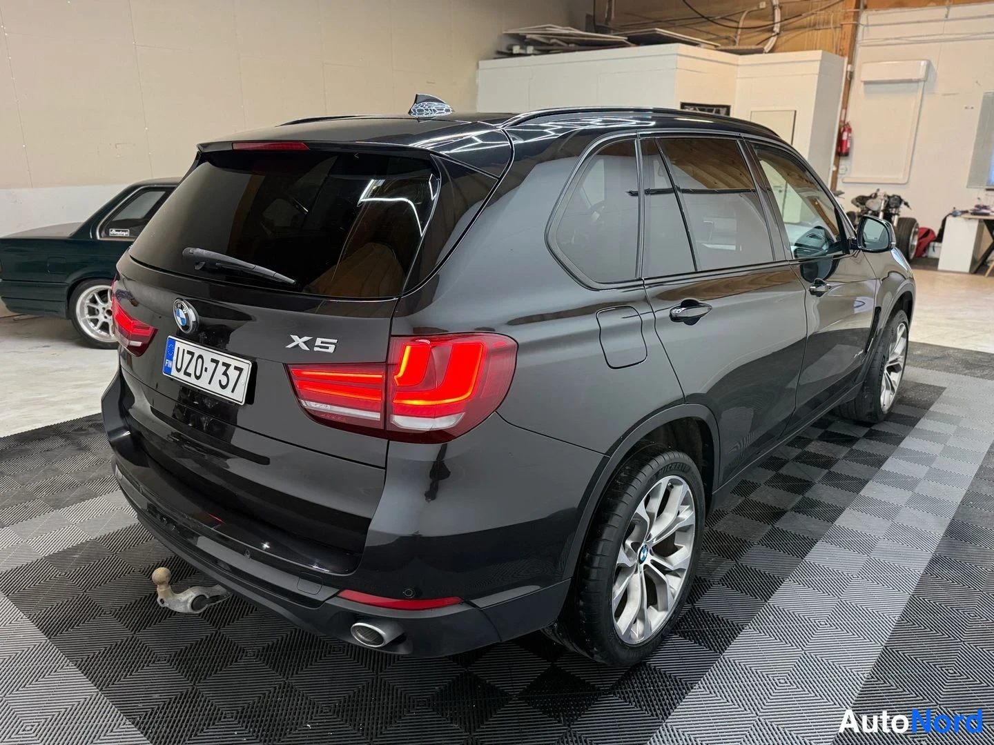 Takaviisto: BMW X5:n takakulma vasemmalta takaa kuvattuna; kannessa X5-merkki ja rekisteritunnus, takakiinnityksessä vetoautohaken.
