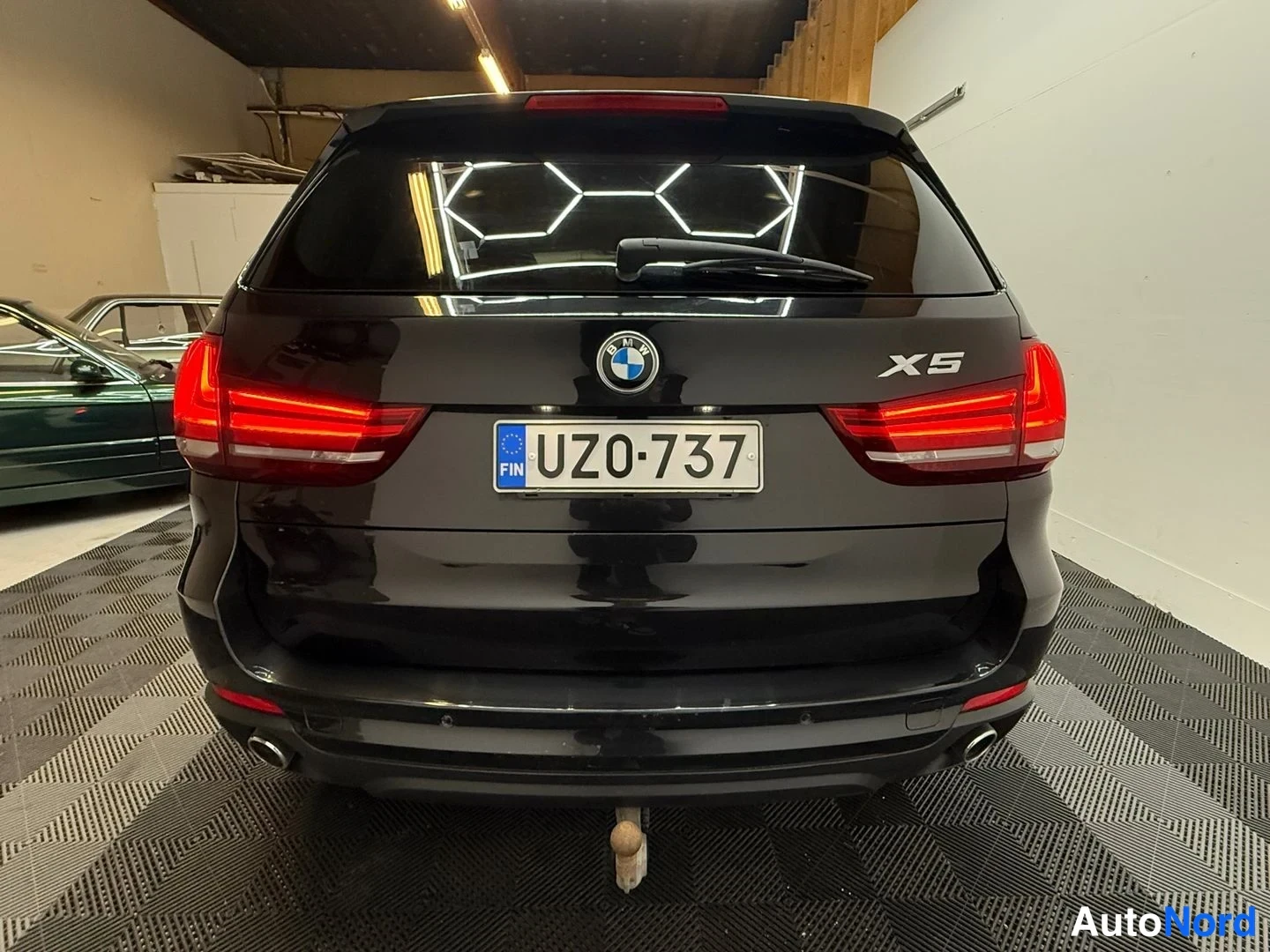 Takaa: Mustan BMW X5:n takaosa, rekisterikilpi, takavetovaljaat ja vetokoulu näkyvissä.