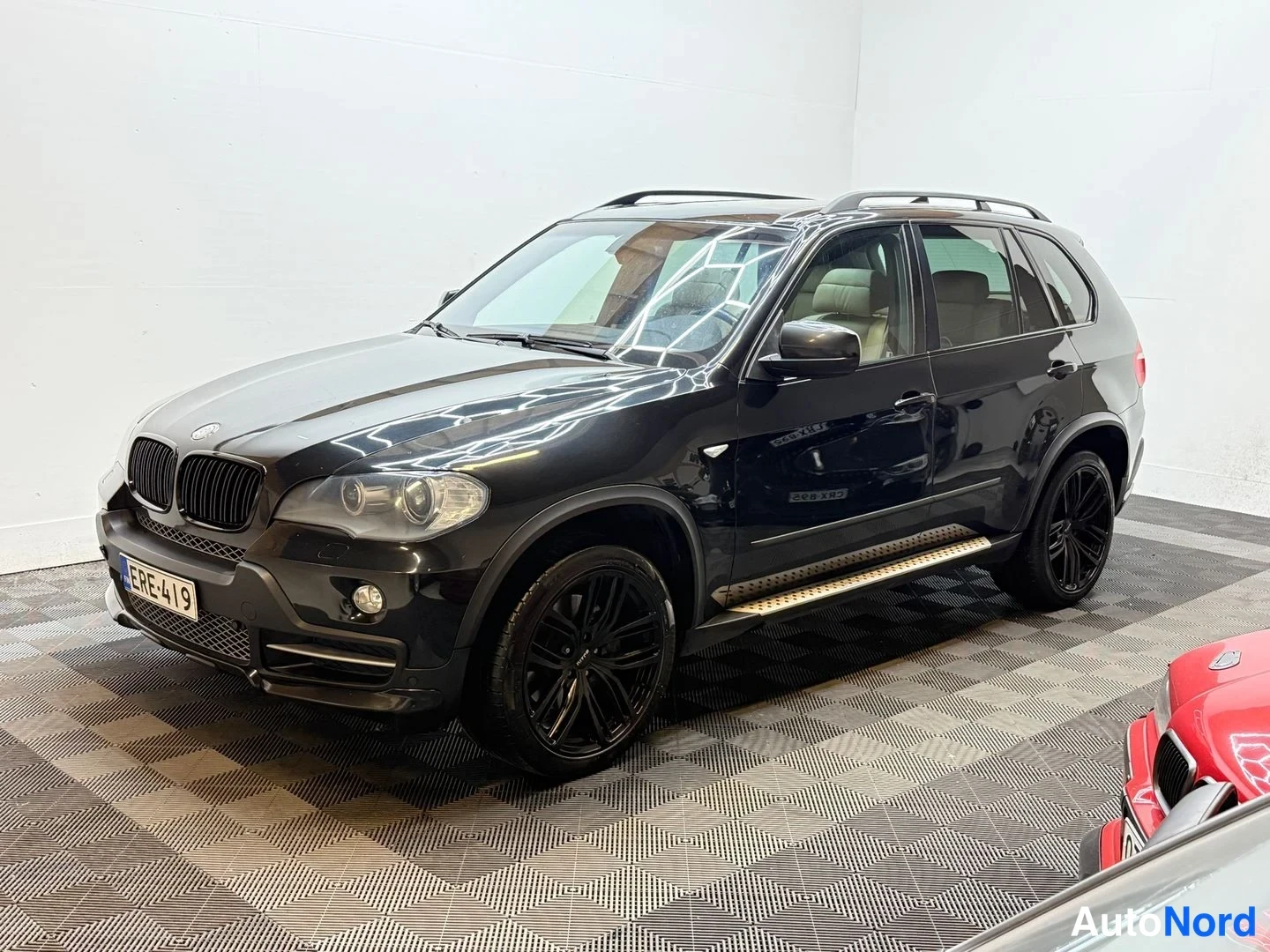 Etuviisto, nokka vasemmalle: Musta BMW X5 -maastauto etuviistosta vasemmalle, roof rails ja mustat vanteet näkyvät.