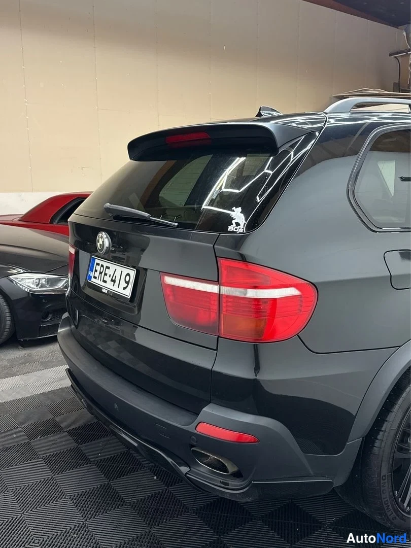 Takaviisto: Mustan SUV-auton takaosa ja takaoikea kylki; rekisterikilpi, punaiset takavalot, takanäkyvyysovi ja pakoputki erottuvat.