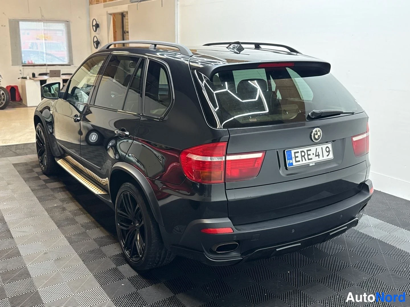 Takaviisto: BMW takaa ja sivulta vasemmalta, kattotelineet ja tummat vanteet