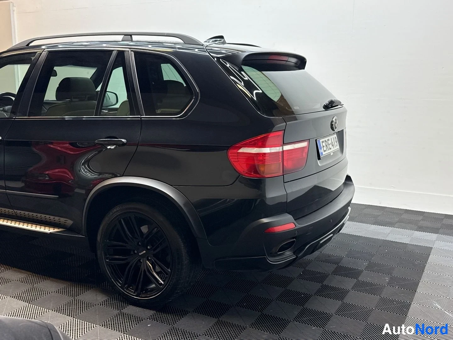 Takaviisto: BMW X5:n takaosa ja vasen kylki kolmannelta neljännekseltä, musta maali, taustavalot ja rekisterikilpi näkyvissä.