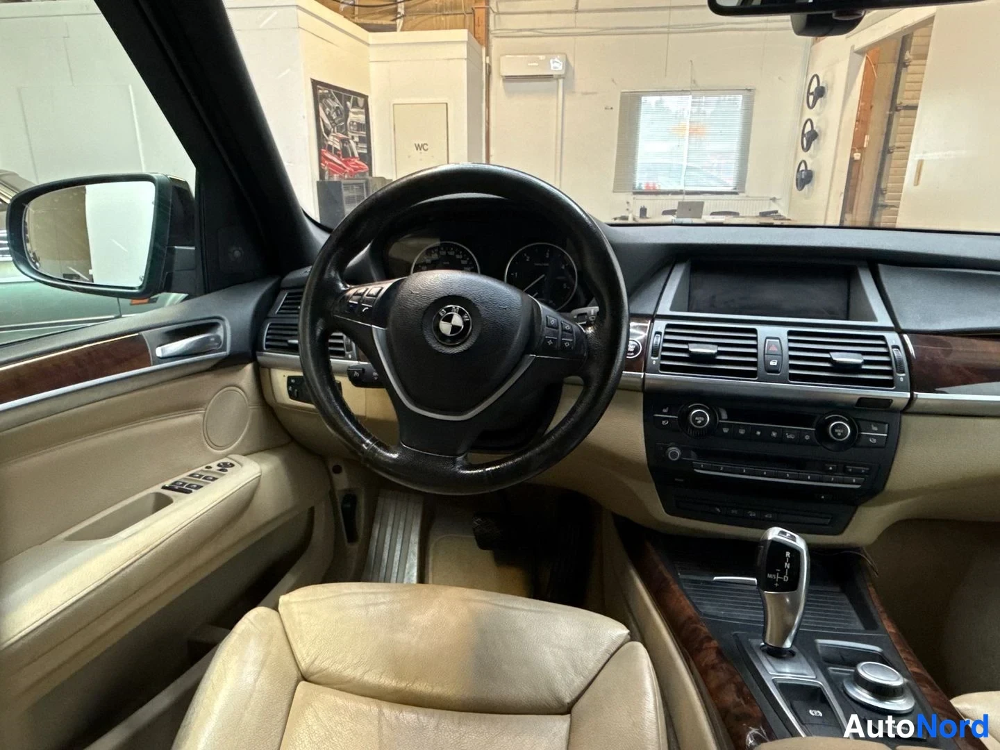 Muu: BMW X5:n ohjaamon vasen etuosa: BMW-merkkinen ohjauspyörä, mittaristo ja beigea nahkaa.