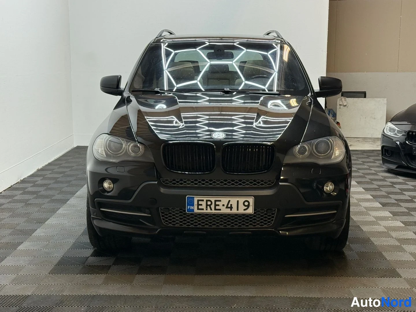 Edestä: Musta BMW X5 suoraan edestä, kilpi, kaksois munuaiset ja sumuvalot.