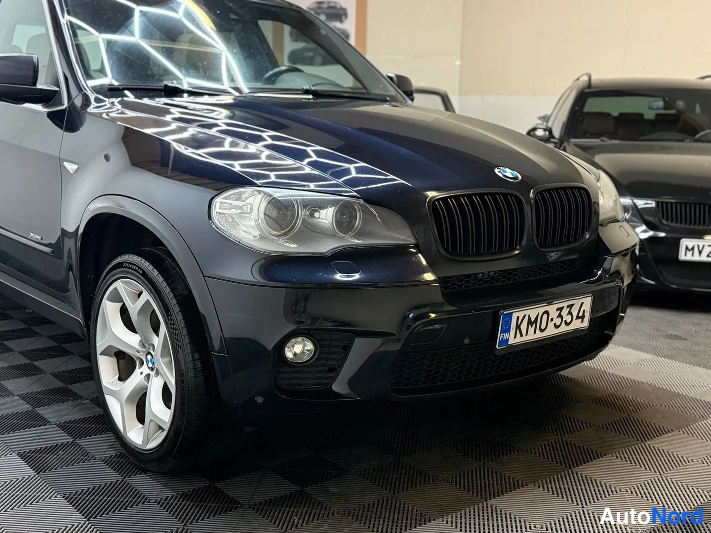 Etuviisto, nokka oikealle: Tumman BMW X5:n etukulma lähikuvassa, etupyörä ja etusäleikkö näkyvät, rekisteritunnus KM0-334