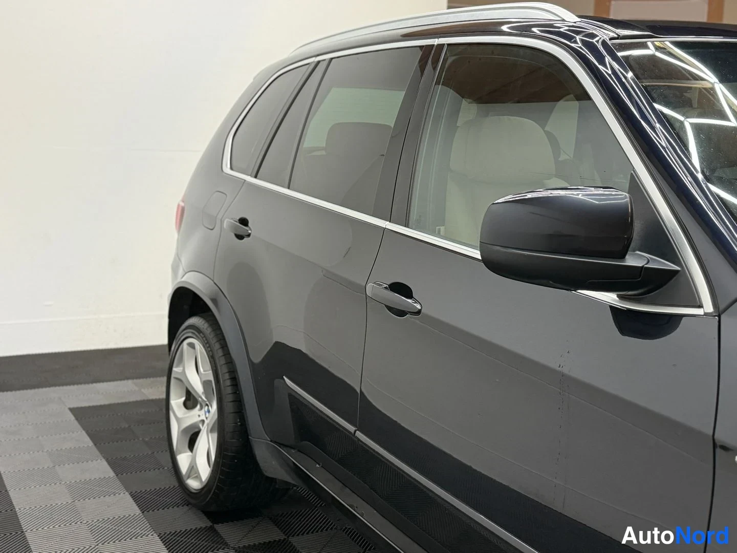 Sivulta: Tumman BMW X5:n sivuprofiili, kaksi ovea, takapenkku ja kirkas katossa ja istuimissa