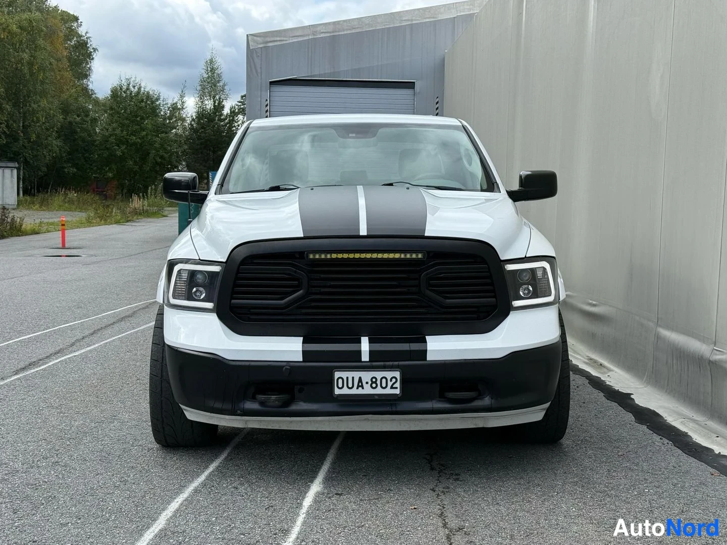 Edestä: Valkoinen pickup-auto suoraan edestä, mustat peltiritilät ja konepellin mustat raidat, LED-palkki konepellin yllä.