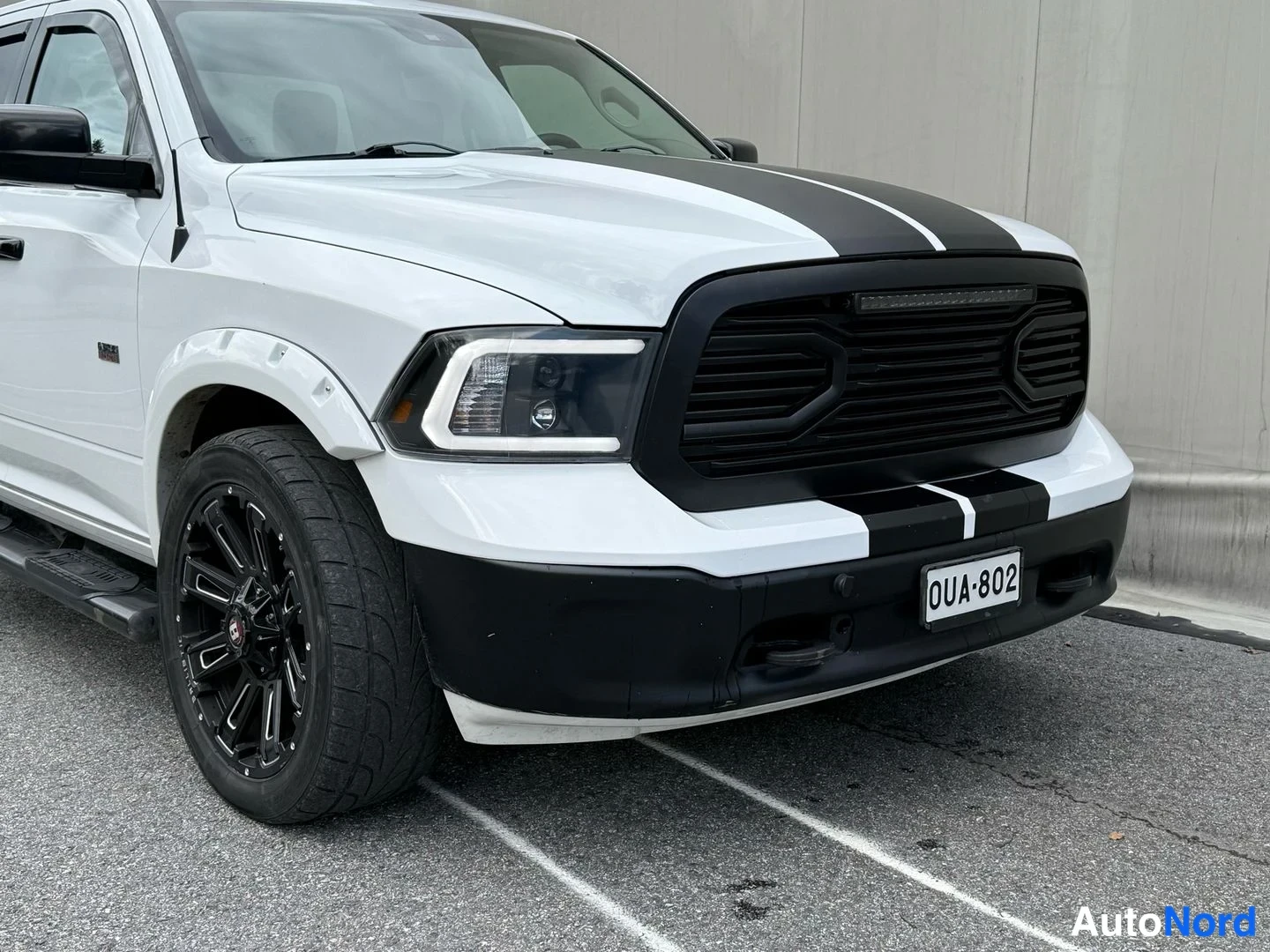 Etuviisto, nokka oikealle: Valkoinen Dodge Ram -nosturi edestä oikealta kuvattuna; musta etusäleikkö, LED-ajovalot ja mustat vanteet, rekisteritunnus.