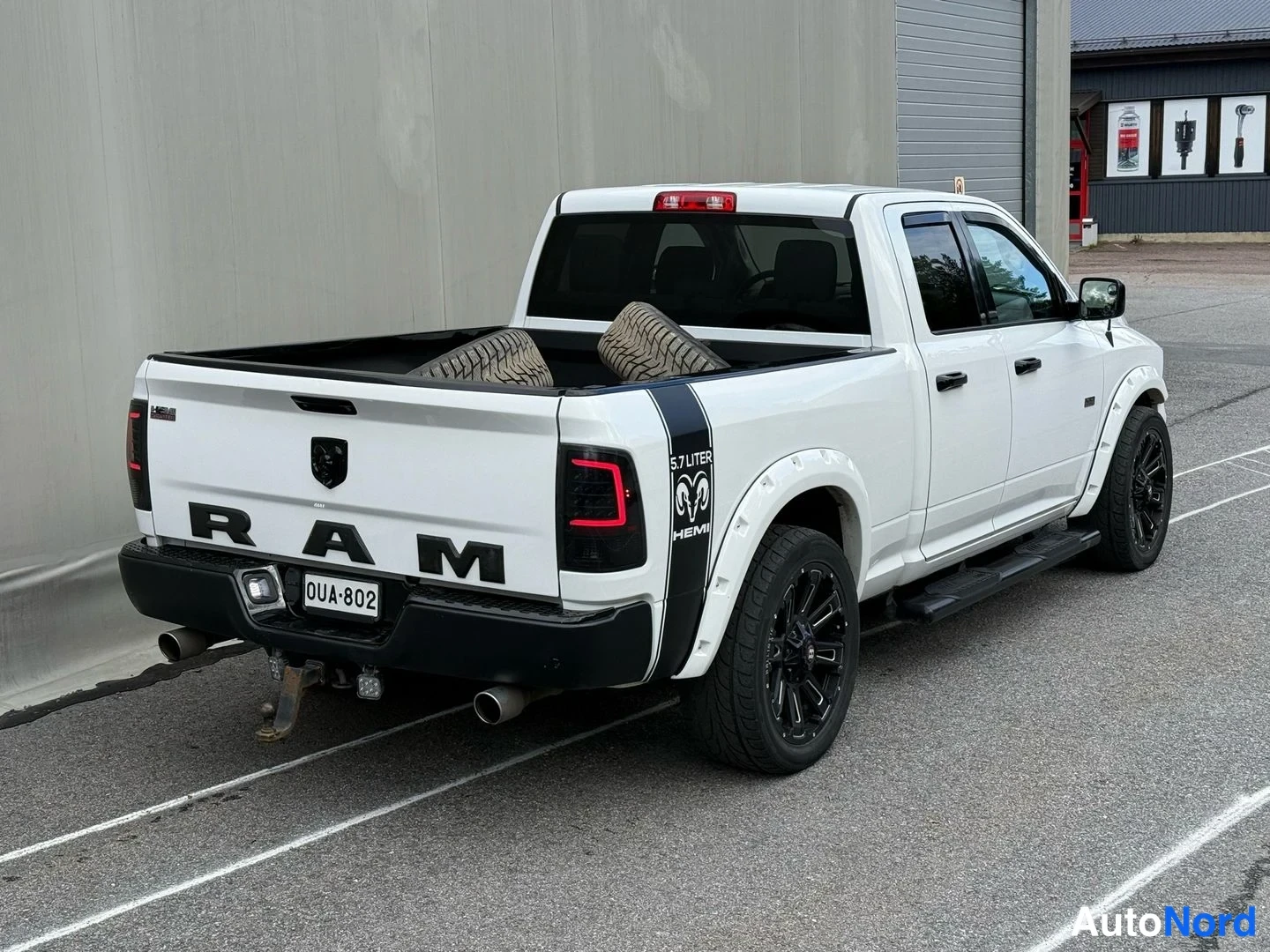 Takaviisto: Valkoinen Dodge Ram -nosturi takaa oikealta kuvattuna; RAM-teksti kannessa, mustat takavalot ja savuputket, rekisteritunnus.
