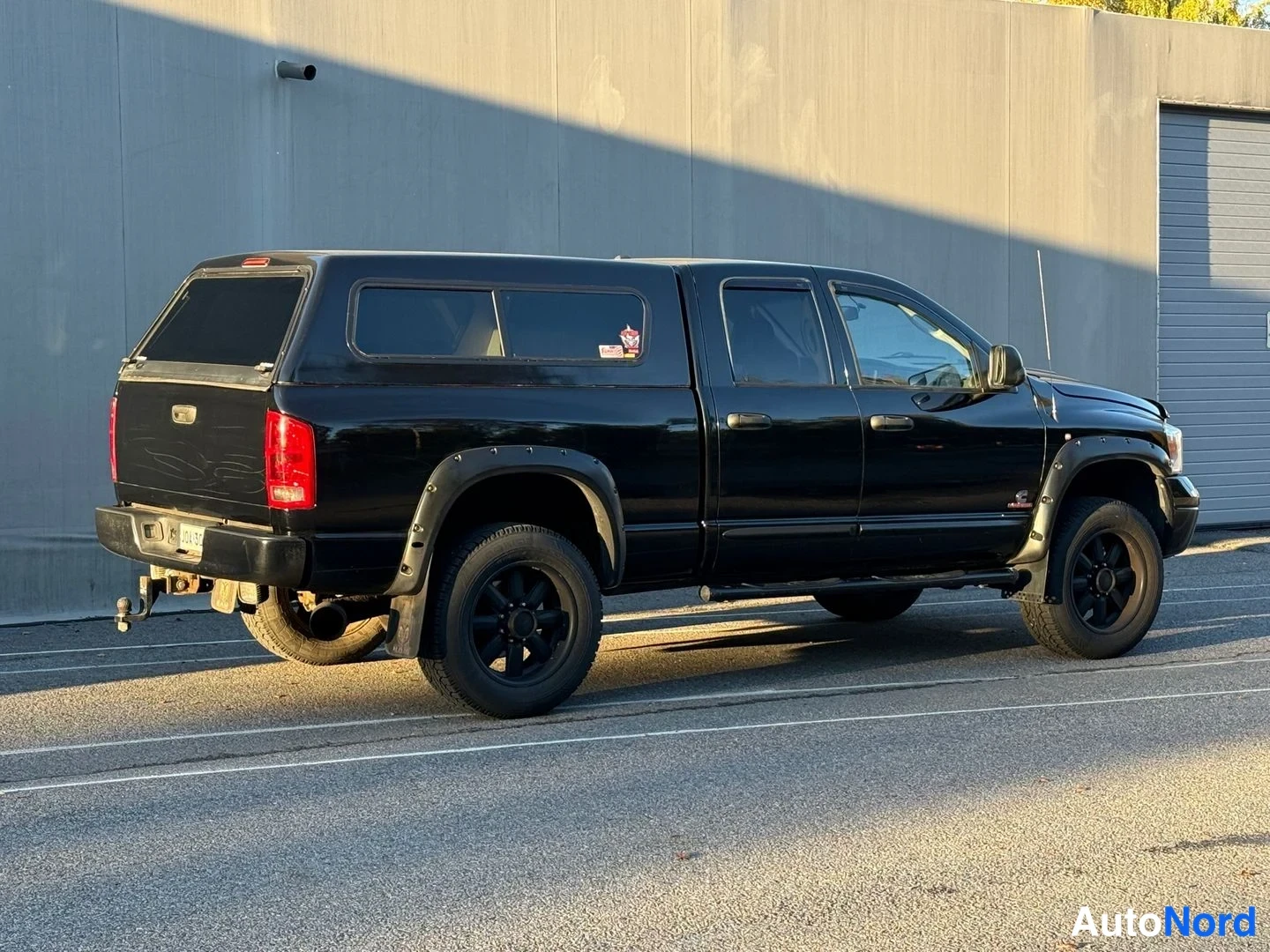Takaviisto: Musta Dodge Ram -avolava takaa kolmessa neljäsosassa vasemmalta, takavalot ja lava näkyvissä, lavalla tumma kuormatilan kate.