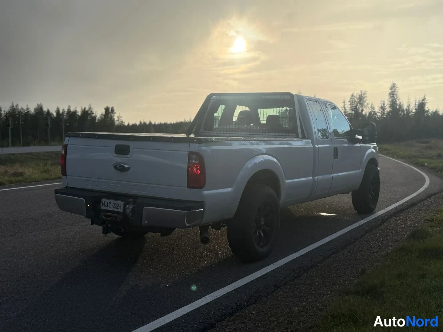 Takaviisto: Valkoisen pickupin takakulmanäkymä toisesta suunnasta aurinkoisen tien varrella, takapuoli ja oikea kylki näkyvät.