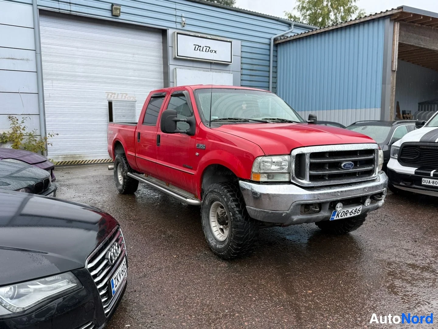 Etuviisto, nokka oikealle: Punainen Ford F-350 avolava etukulmasta oikealta päin piha-alueella, rekisterikilpi.