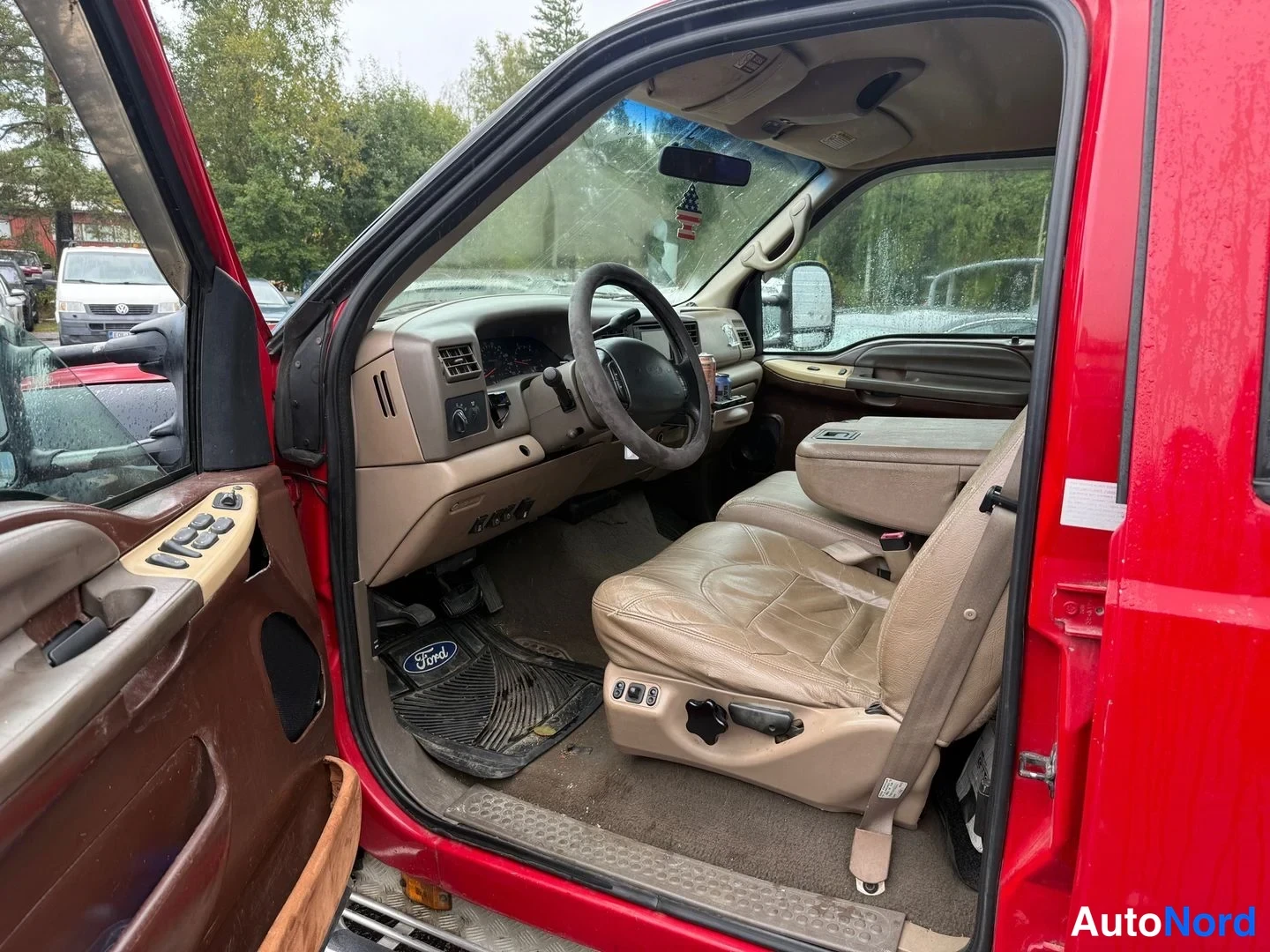 Etuviisto, nokka oikealle: Ford F-350:n sisätila kuljettajan ovi auki: beigea nahkapenkkia ja kojelautaa, lattiamatossa Ford-logo.