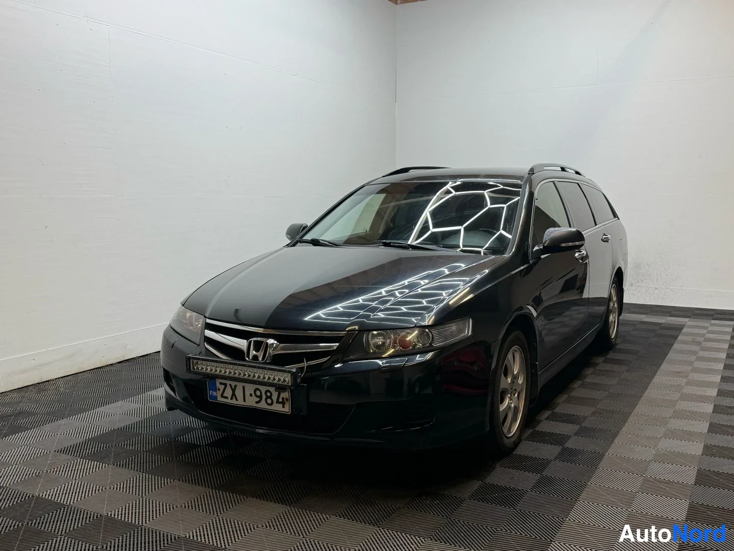 Etuviisto, nokka vasemmalle: Honda Accord -farmarin etukulmakuva hieman sivulta: musta koriväri, tuulilasissa valaistuksen heijastuksia, kilpi