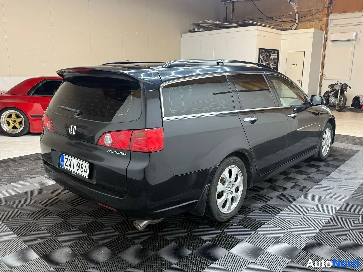 Takaviisto: Musta Honda Accord Tourer -farmari kuvattu kolmeneljännesnäkymässä takaosasta vasemmalta näkyen; takavalojen punaiset osat ja rekisterikilpi näkyvät.