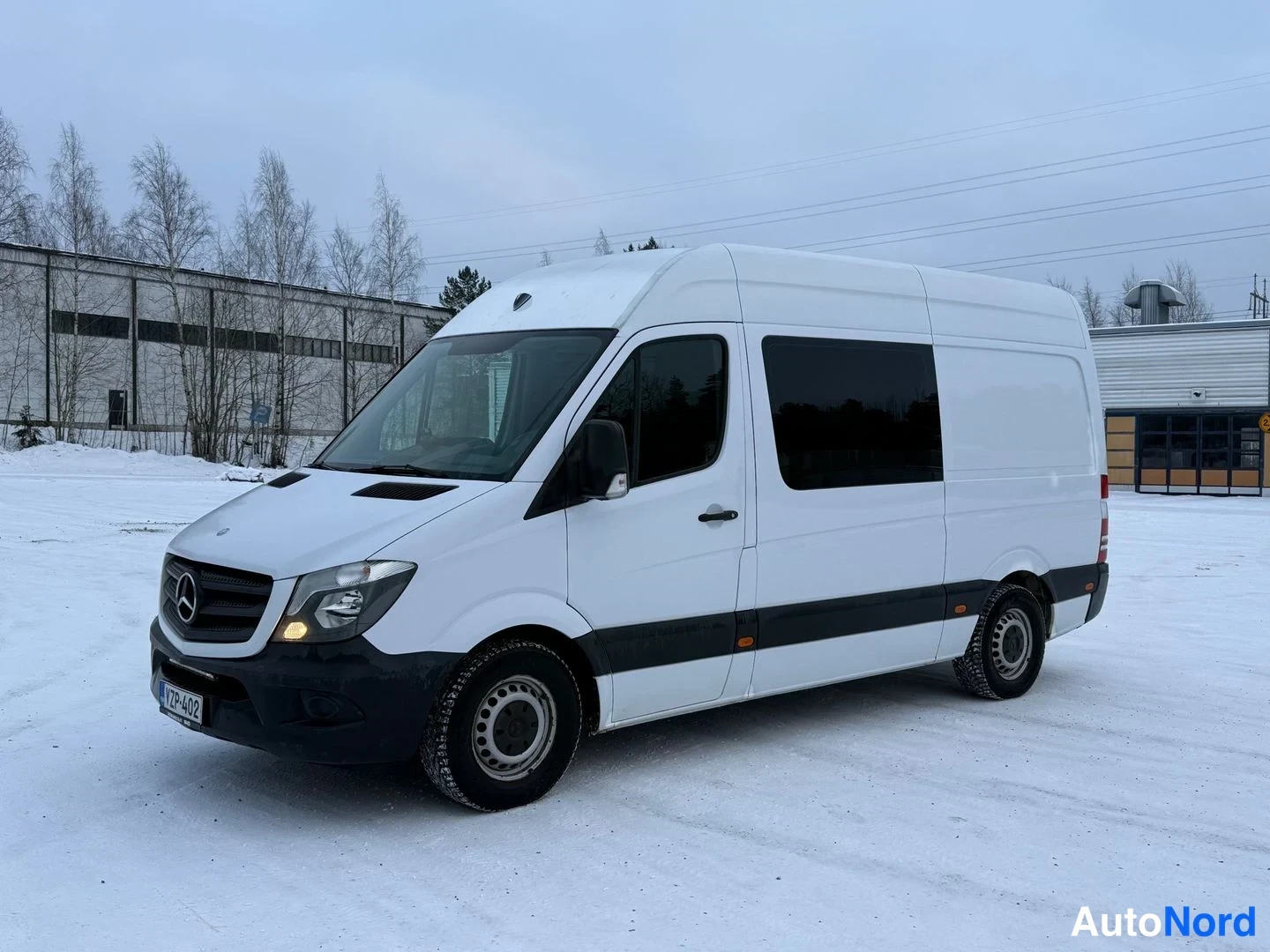 Etuviisto, nokka vasemmalle: Valkoinen Mercedes-Benz Sprinter -pakettiauto etuviistossa vasemmalta lumisella parkkipaikalla.