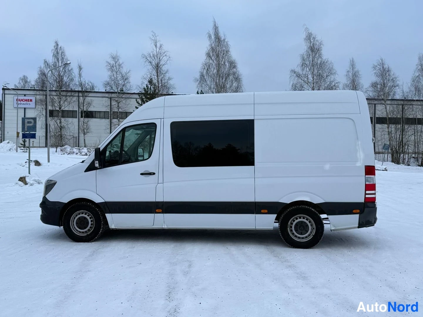 Etuviisto, nokka vasemmalle: Mercedes-Benz Sprinter -pakettiauton kylki sivulta, valkoinen kori, tumma sivulistike ja talvimaisema.