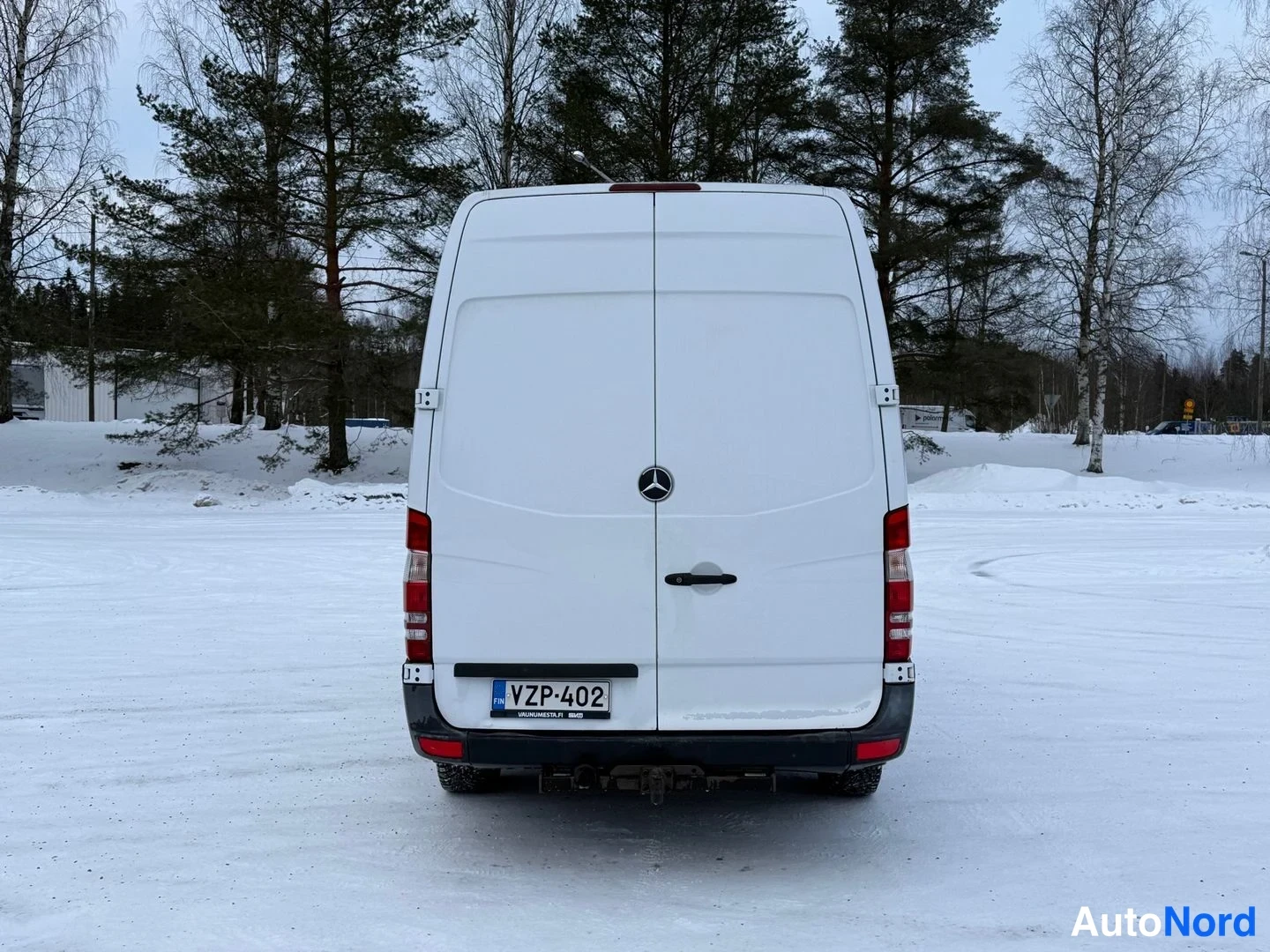 Takaa: Mercedes-Benz Sprinter -pakettiauton takaosa lumialueella, valkoinen kori ja rekisterikilpi.