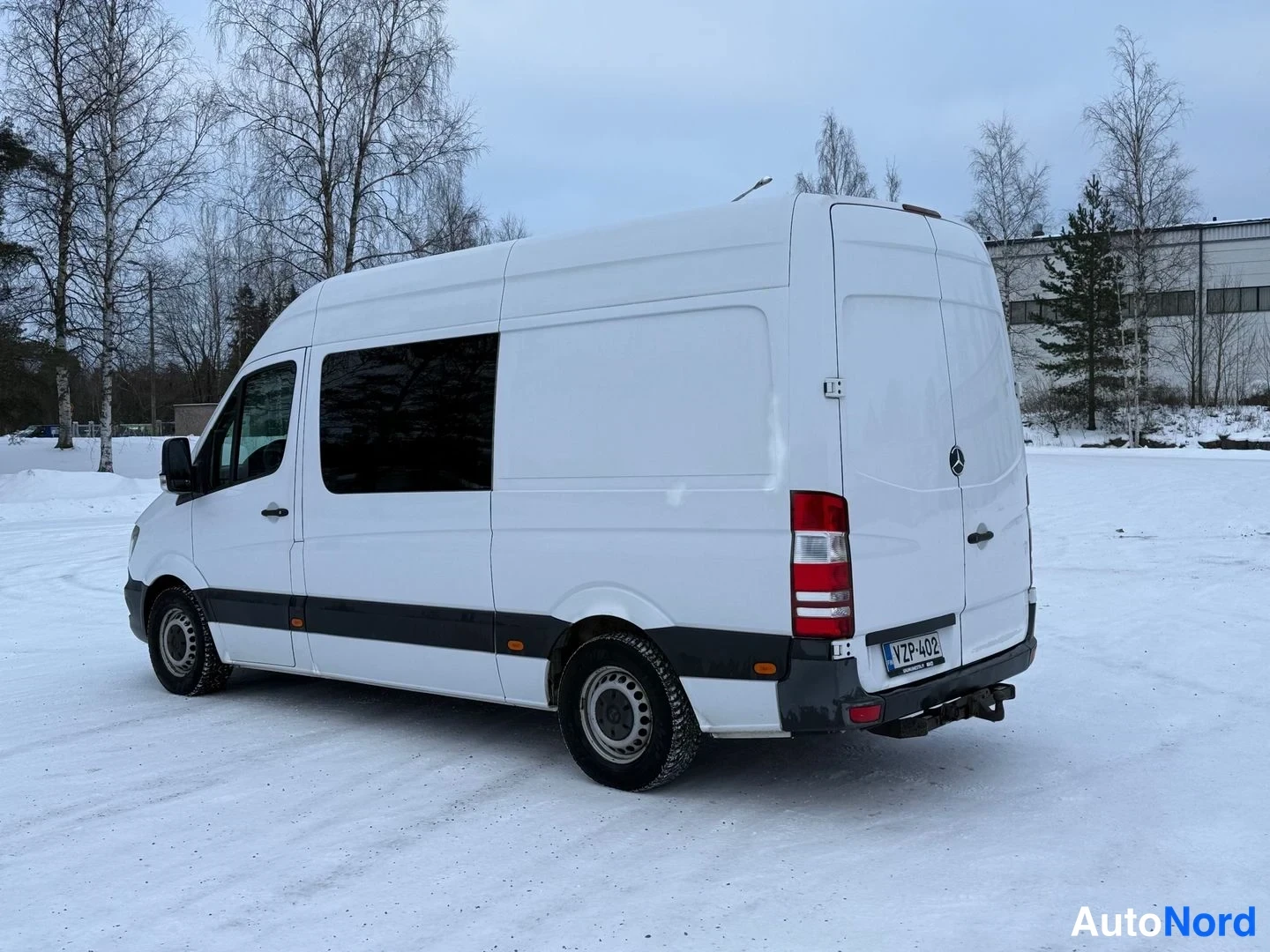 Takaviisto: Mercedes-Benz Sprinter -pakettiauto kolmesta neljäsosaa takaa, valkoinen kori, tummat sivuikkunat ja lumipeitteinen tausta.