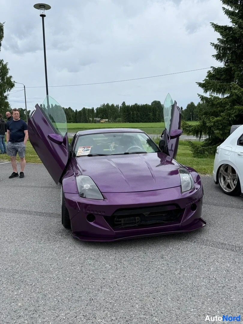 Edestä: Violetti Nissan 350Z edestäpäin; molemmat ovit on avattu ylöspäin siipiovin, konepellin kulmat ylös ja iso etusplitteri. Kylkillä on leveät lokasuojat.
