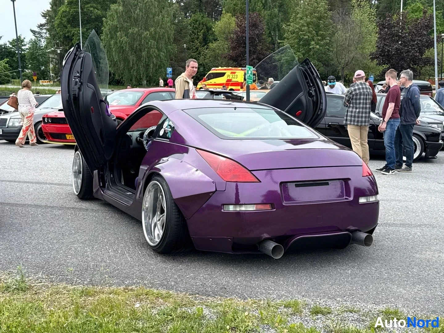 Takaviisto: Violetti Nissan 350Z takaa vasemmalta sivulta kuvattuna; siiviovet ovat auki ylös, isot hopeavanteet, kaksoispaalupakoputket ja leveät lokasuojat näkyvät. Taust