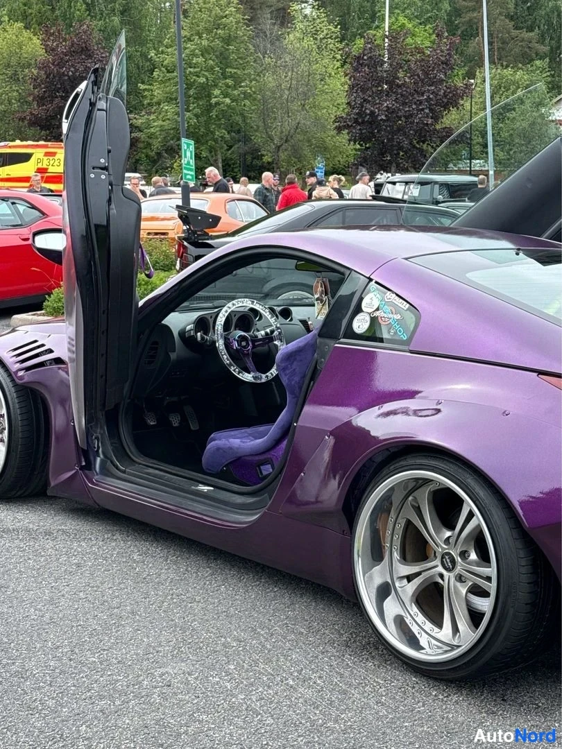 Sivulta: Violetin purppuranvärinen urheiluauto sivulta kuvattuna, kuljettajan ovi ylhäällä auki ja sisällä vihreä-sininen ohjauspyörä sekä tummat istuimet.