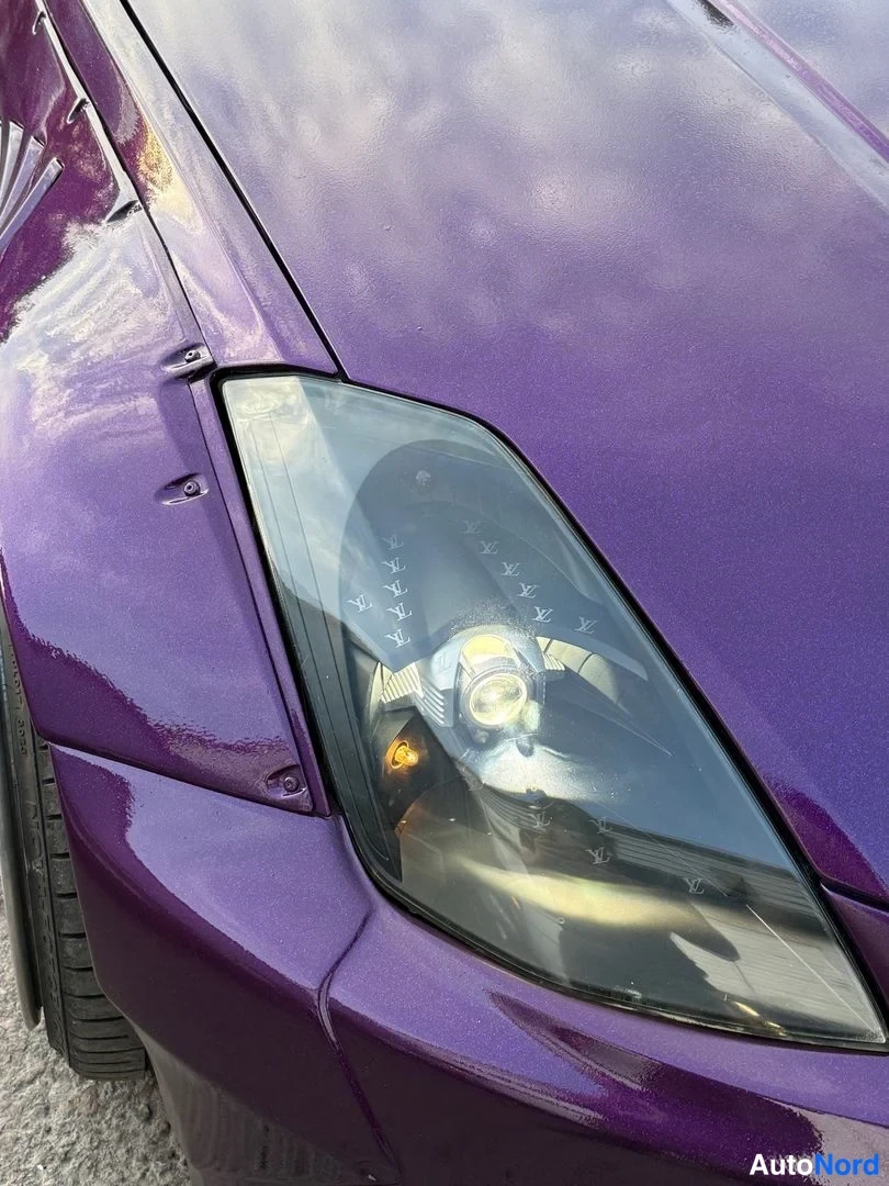 Edestä: Lähikuva auton etuaisen ajovalaisimesta ja violetista konepellistä.