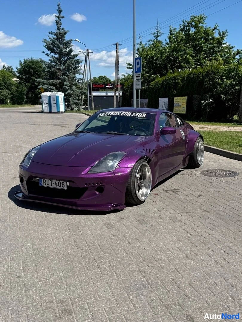 Etuviisto, nokka vasemmalle: Violetti Nissan 350Z -coupe etuviistosta; konepellillä ja tuulilasissa Rocket Bunny -tekstejä, rekisteri.