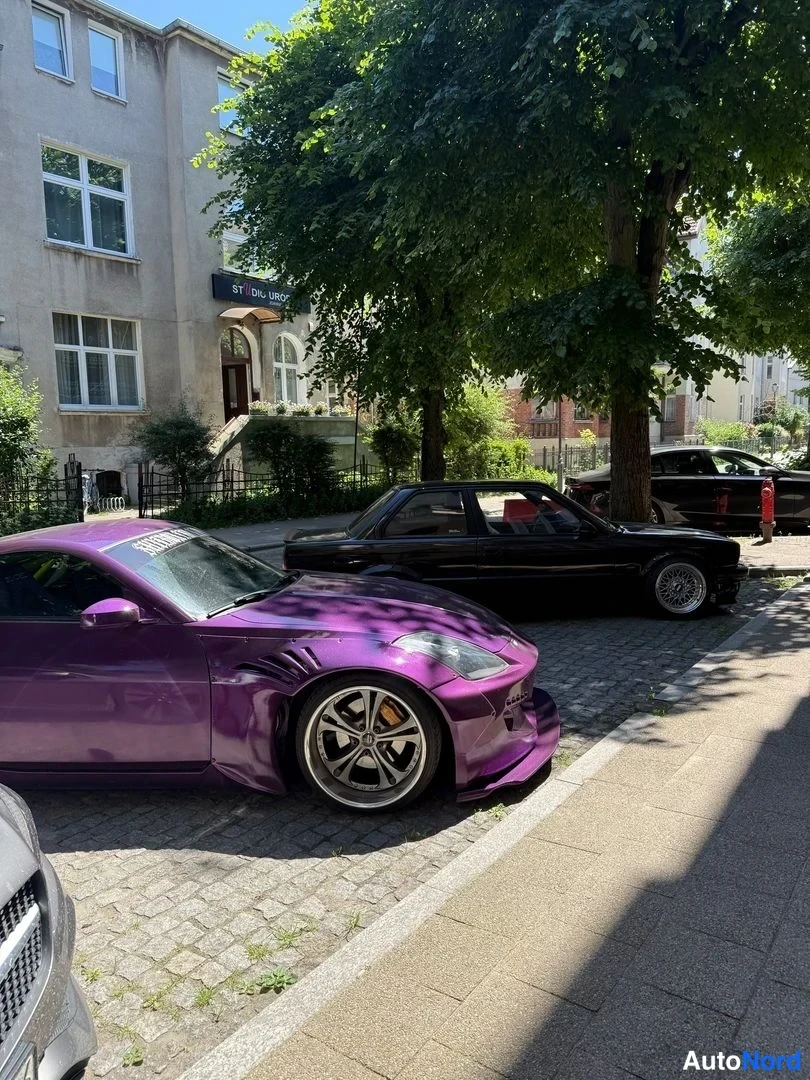 Etuviisto, nokka oikealle: Violetti urheiluauto seisoo kadunvarrella, etukulma oikealle, leveät lokasuojat ja tummat vanteet.