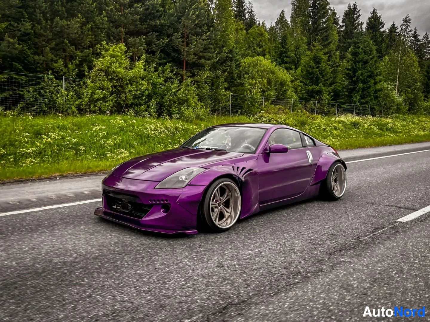 Edestä: Violetti Nissan 350Z urheiluauton etukulma vasemmalta ajettaessa tiellä, matala etuspoileri ja muokattu levyinen runko.