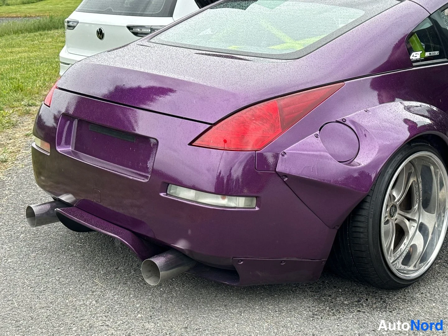 Takaviisto: Violetin pysäköity Nissan 350Z takaa oikealta sivulta kuvattuna; leveä takalokasuoja, isot hopeavanteet, punaiset takavalot ja kaksoispaalupakoputki näkyvät. Ka