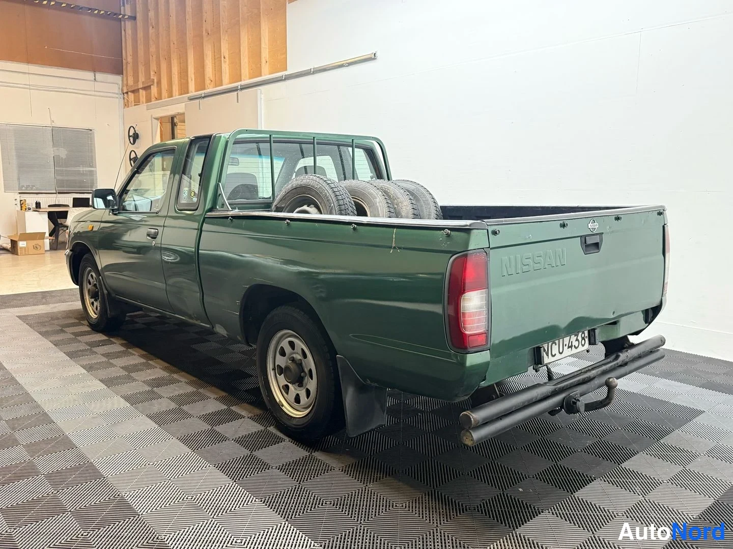 Takaviisto: Vihreä avolava-auto takana ja sivulta, lavassa renkaita, takapaneelissa NISSAN-teksti, rekisteri.